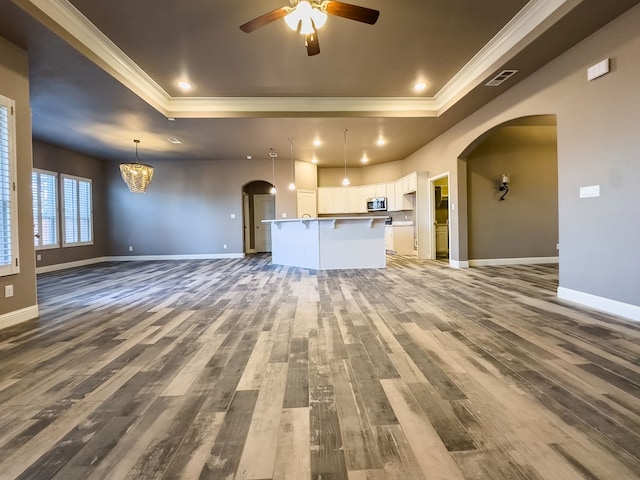 unfurnished living room with a raised ceiling, hardwood / wood-style floors, ceiling fan with notable chandelier, and ornamental molding