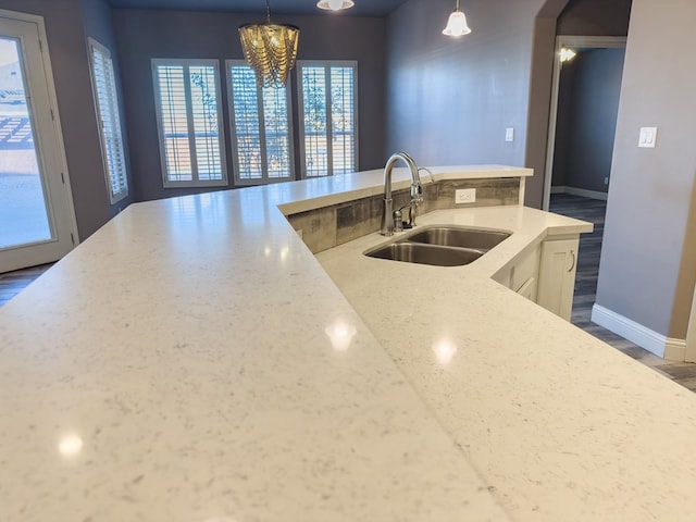 kitchen with light stone counters, sink, pendant lighting, and an inviting chandelier