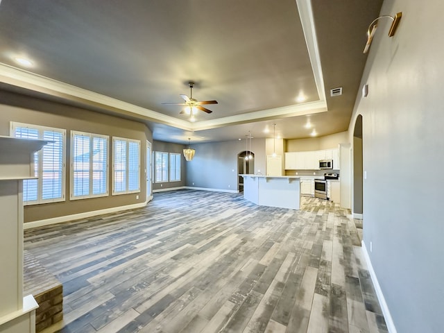 unfurnished living room featuring a raised ceiling, hardwood / wood-style floors, ceiling fan with notable chandelier, and ornamental molding