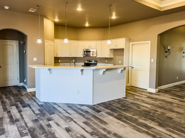 kitchen featuring white cabinets, stainless steel appliances, hanging light fixtures, and an island with sink