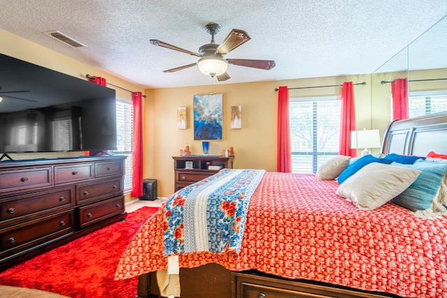 bedroom featuring carpet flooring, a textured ceiling, multiple windows, and ceiling fan