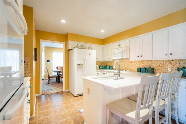 kitchen with white appliances, a textured ceiling, tasteful backsplash, a kitchen bar, and white cabinetry