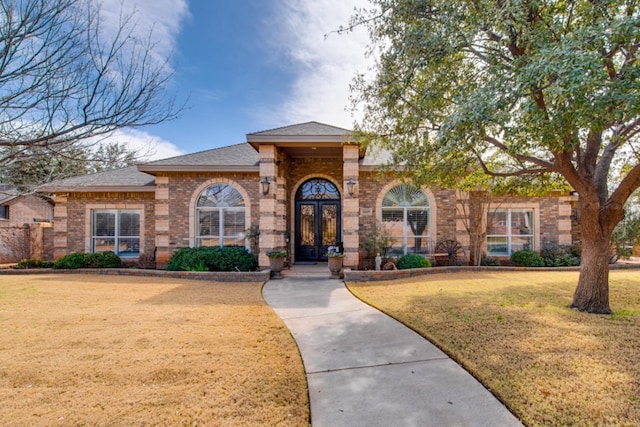 view of front of home with brick siding, roof with shingles, french doors, and a front yard