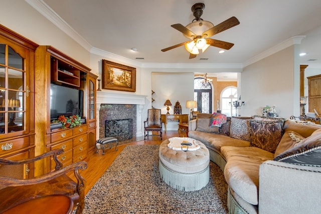 living area with ceiling fan, a fireplace with flush hearth, wood finished floors, visible vents, and crown molding