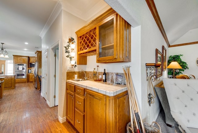 kitchen with ornamental molding, brown cabinetry, glass insert cabinets, a sink, and light wood-type flooring