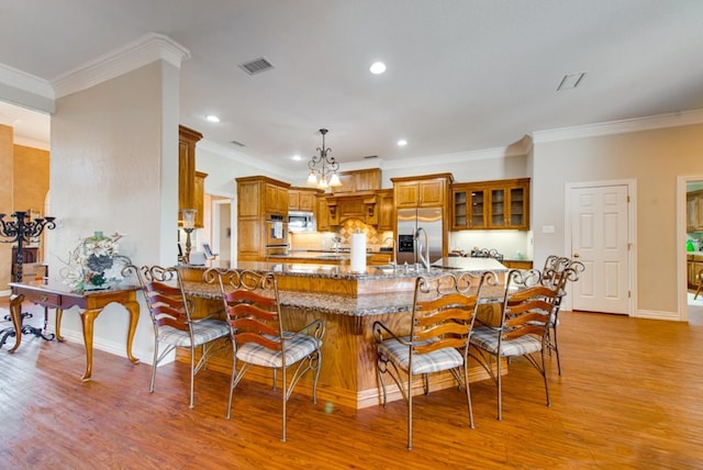 kitchen with light wood finished floors, visible vents, brown cabinetry, appliances with stainless steel finishes, and a breakfast bar