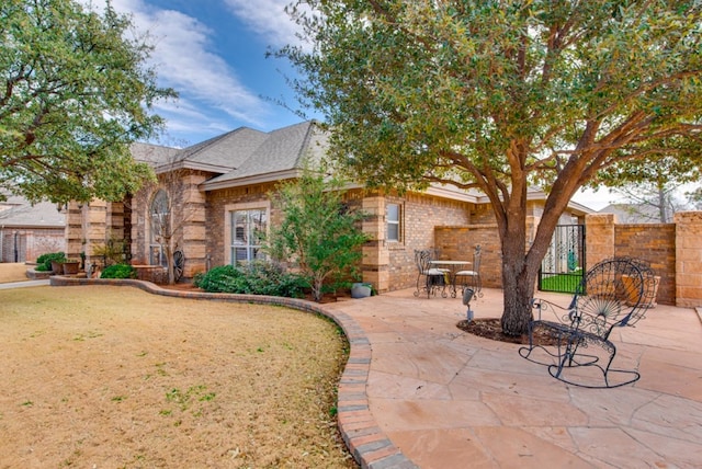 view of front of property featuring a patio area, stone siding, fence, and brick siding