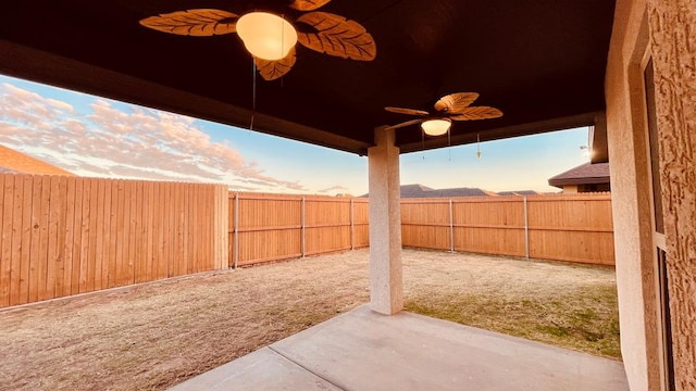 yard at dusk featuring ceiling fan and a patio area