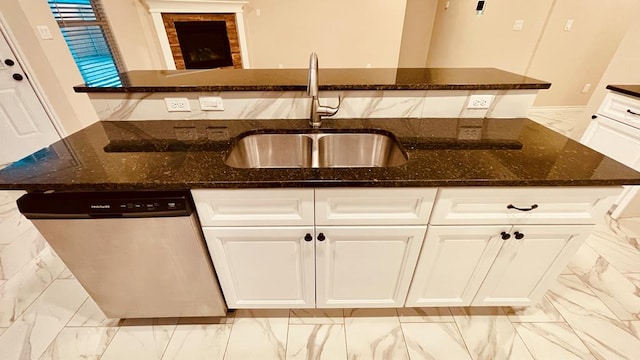 kitchen with stainless steel dishwasher, a center island with sink, and dark stone counters