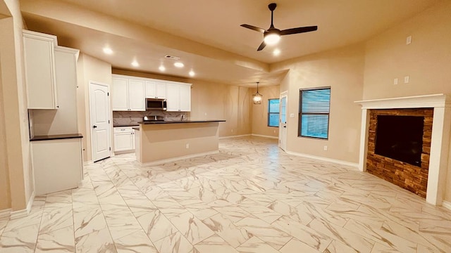 kitchen with a stone fireplace, ceiling fan, a kitchen island, white cabinetry, and backsplash