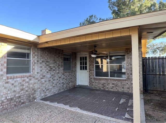 entrance to property featuring a ceiling fan, brick siding, fence, and a patio