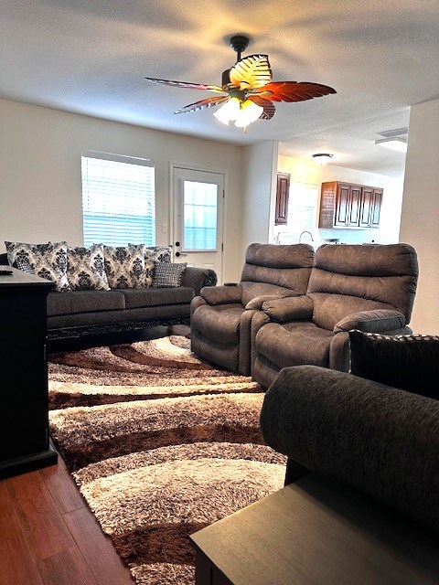 living room featuring dark hardwood / wood-style floors, ceiling fan, and a textured ceiling