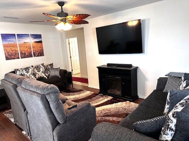 living room with a textured ceiling, ceiling fan, a fireplace, and dark hardwood / wood-style floors