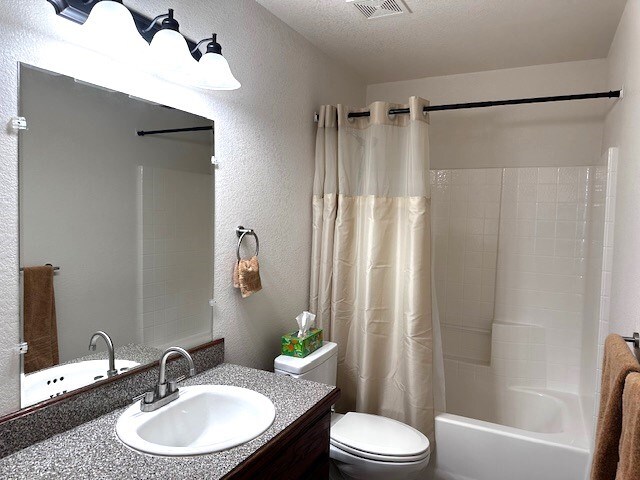 full bathroom with a textured ceiling, vanity, toilet, and shower / bathtub combination with curtain