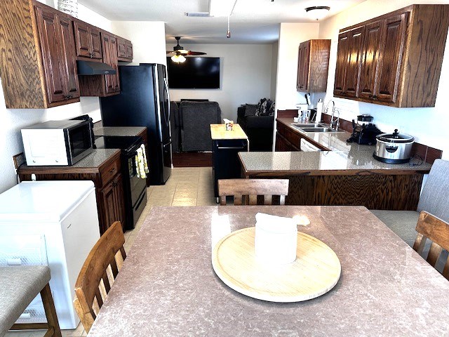 kitchen featuring kitchen peninsula, dark brown cabinets, sink, light tile patterned floors, and black electric range oven