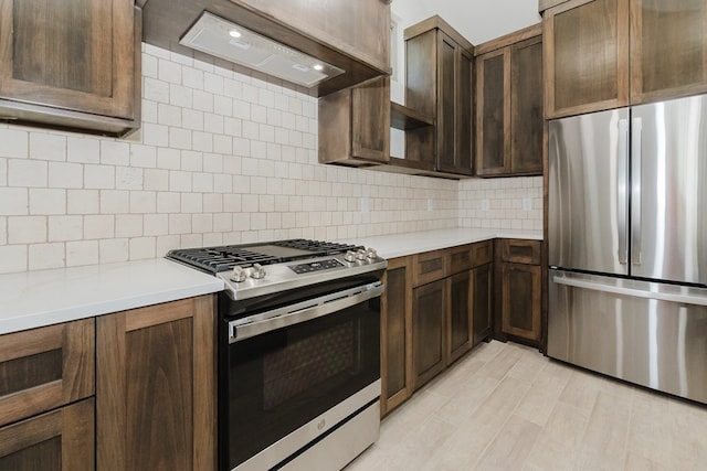 kitchen with dark brown cabinetry, light hardwood / wood-style flooring, premium range hood, backsplash, and appliances with stainless steel finishes