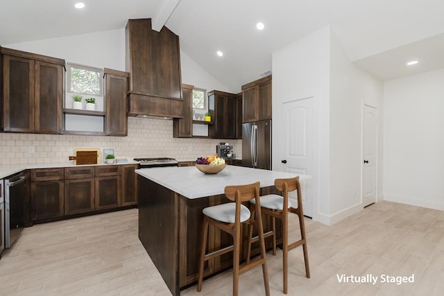 kitchen with light wood-type flooring, custom exhaust hood, stainless steel appliances, lofted ceiling with beams, and a center island