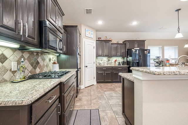 kitchen featuring decorative light fixtures, tasteful backsplash, a kitchen island with sink, black appliances, and dark brown cabinets