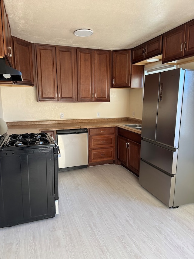 kitchen featuring ventilation hood, light wood-type flooring, a textured ceiling, and appliances with stainless steel finishes