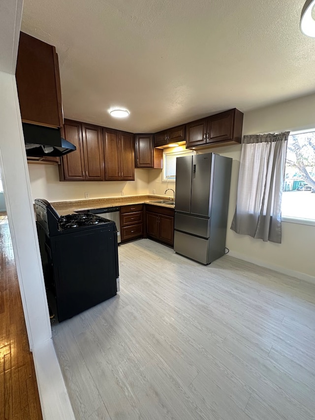 kitchen featuring stainless steel fridge, light wood-type flooring, black gas range oven, and dark brown cabinetry