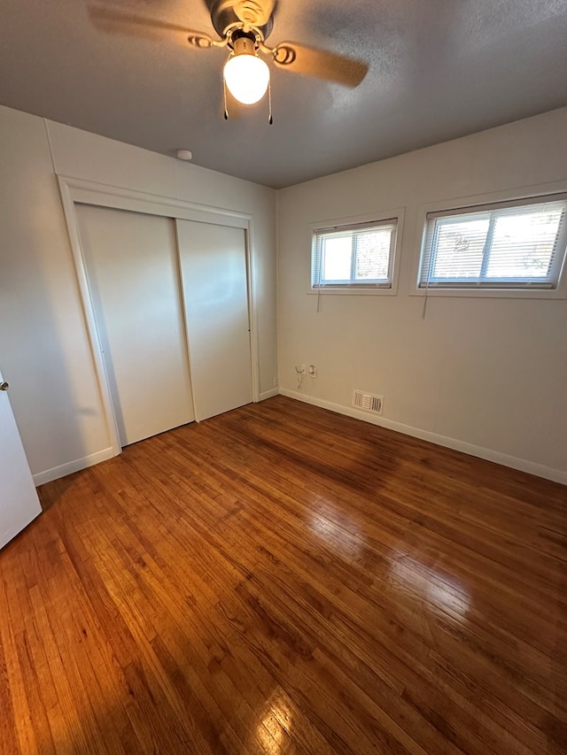 unfurnished bedroom featuring ceiling fan, a closet, dark wood-type flooring, and a textured ceiling