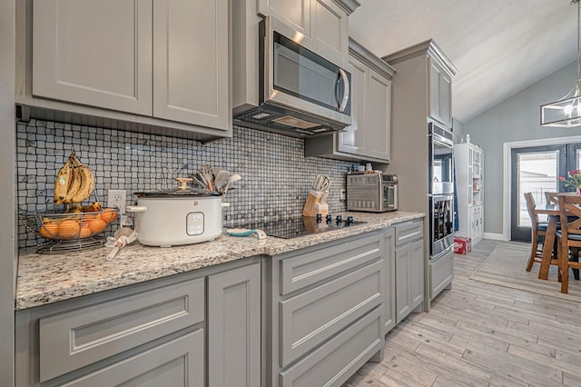 kitchen featuring gray cabinets, pendant lighting, lofted ceiling, light hardwood / wood-style floors, and stainless steel appliances