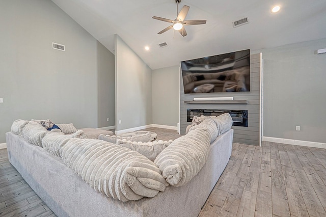 living room with vaulted ceiling, a large fireplace, ceiling fan, and light wood-type flooring