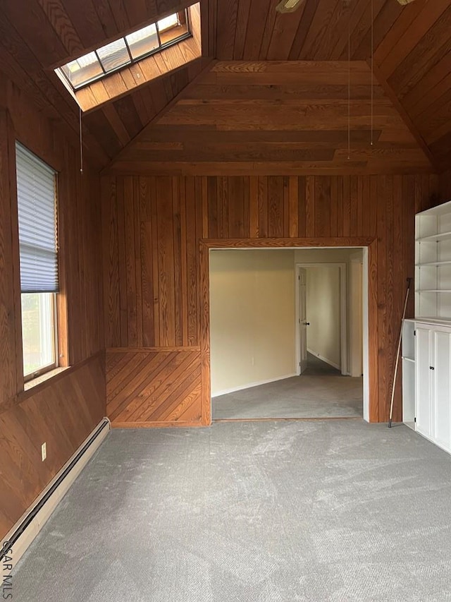 interior space featuring vaulted ceiling with skylight, wood walls, light colored carpet, baseboard heating, and wood ceiling