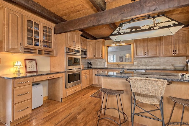 kitchen with glass insert cabinets, a kitchen bar, wood finished floors, stainless steel appliances, and a sink