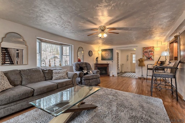 living area featuring a fireplace, a textured ceiling, a ceiling fan, and wood-type flooring