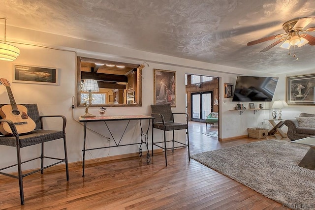 living area featuring a ceiling fan, baseboards, wood-type flooring, and a textured ceiling