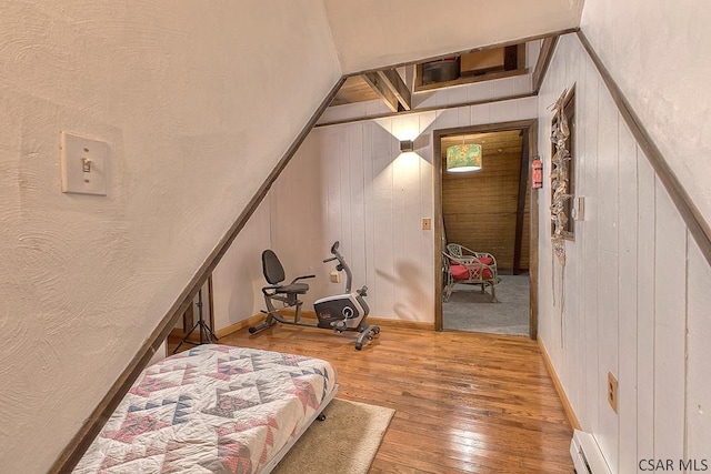 bedroom featuring a baseboard heating unit, baseboards, wood walls, and hardwood / wood-style flooring