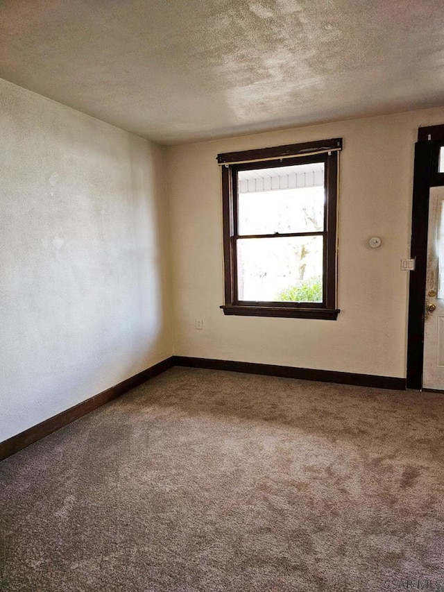 carpeted spare room featuring a textured ceiling and baseboards