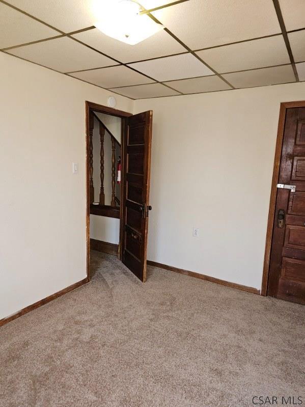 carpeted spare room featuring a paneled ceiling and baseboards