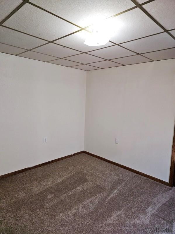 carpeted empty room featuring a drop ceiling and baseboards