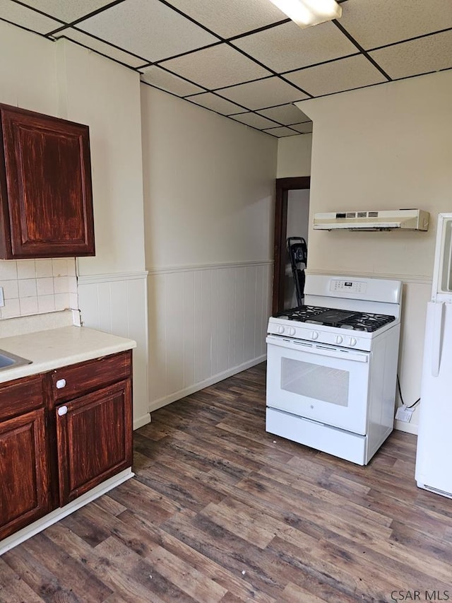 kitchen with under cabinet range hood, a wainscoted wall, white appliances, light countertops, and dark wood finished floors