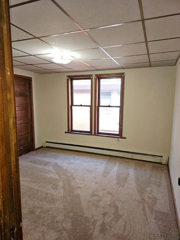 carpeted empty room featuring a baseboard heating unit and a paneled ceiling