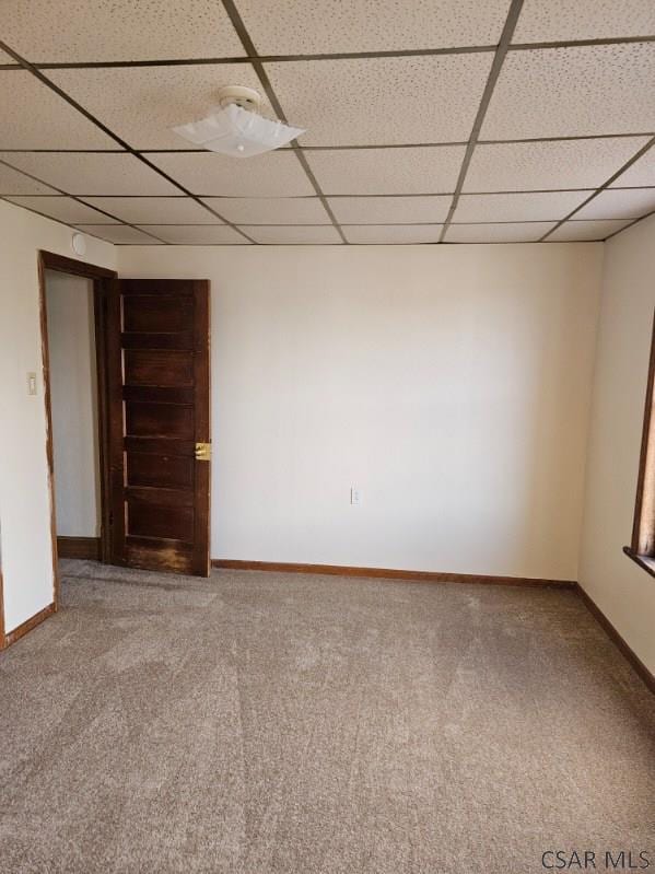 empty room featuring carpet floors, a drop ceiling, and baseboards