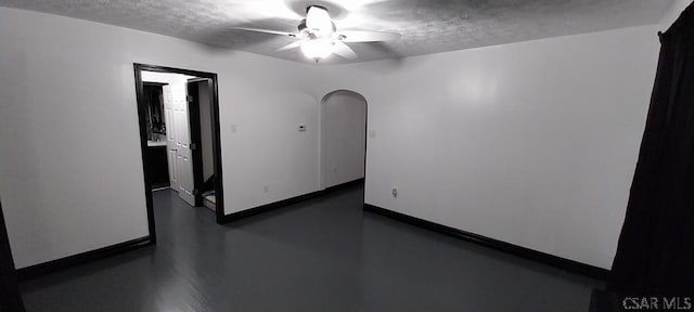 unfurnished room featuring arched walkways, ceiling fan, a textured ceiling, and baseboards