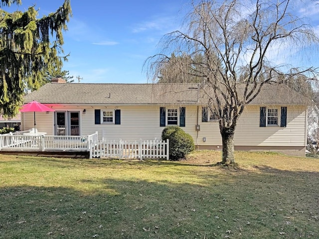 rear view of house with a deck, a chimney, a yard, and a shingled roof