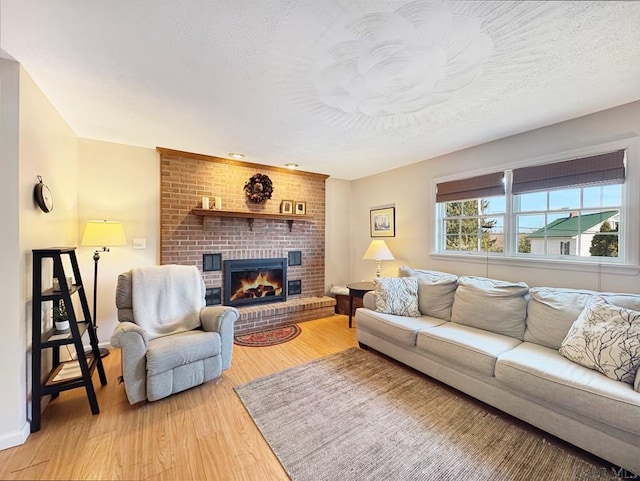 living area with a wealth of natural light, a brick fireplace, a textured ceiling, and light wood-type flooring