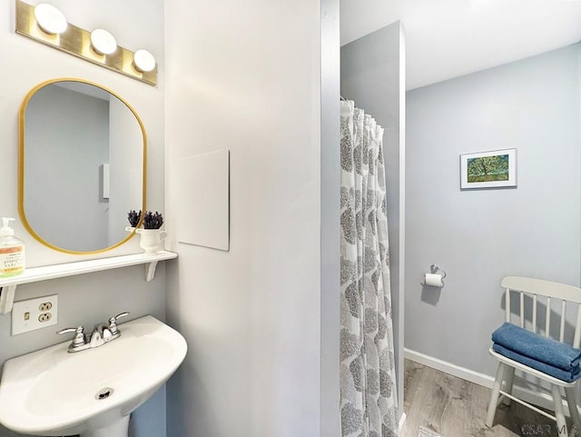 full bath with a shower with curtain, wood finished floors, baseboards, and a sink