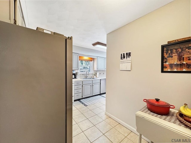 kitchen with light tile patterned flooring, gray cabinets, a sink, light countertops, and appliances with stainless steel finishes