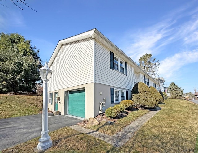 view of side of home featuring aphalt driveway, a garage, a lawn, and stucco siding