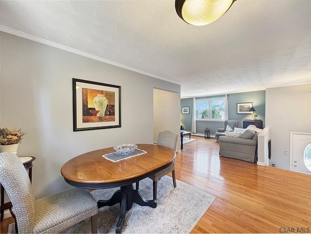 dining space featuring baseboards, light wood-type flooring, and ornamental molding