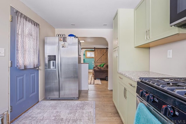 kitchen featuring a barn door, arched walkways, light wood-style flooring, light stone countertops, and stainless steel appliances