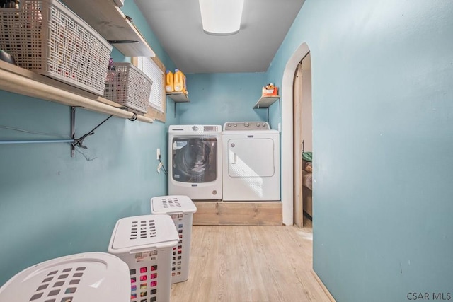 washroom featuring arched walkways, laundry area, washing machine and clothes dryer, and wood finished floors