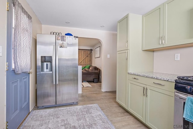 kitchen featuring light stone countertops, light wood-style flooring, arched walkways, and stainless steel appliances