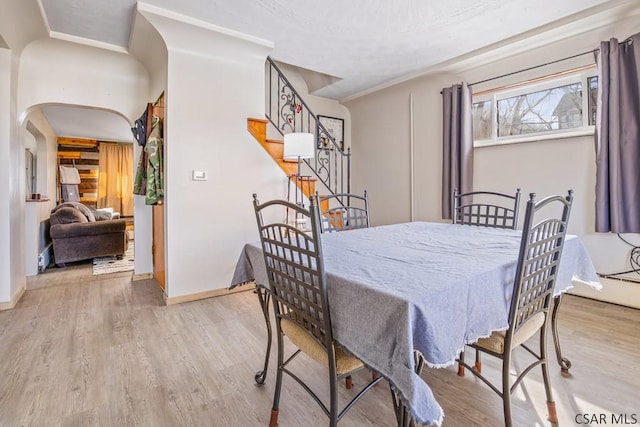 dining space featuring baseboards, stairs, arched walkways, and wood finished floors