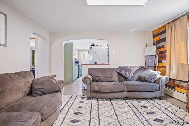 living room with arched walkways, a baseboard radiator, and light wood-style floors